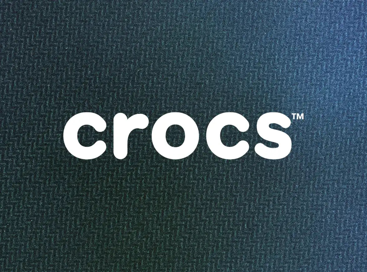 A close-up of the white Crocs logo on a textured, dark background.